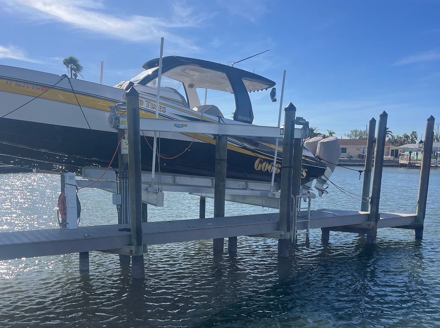 Boat on a lift in a marina. Blue, white, and yellow boat. Clear water, sunny day.