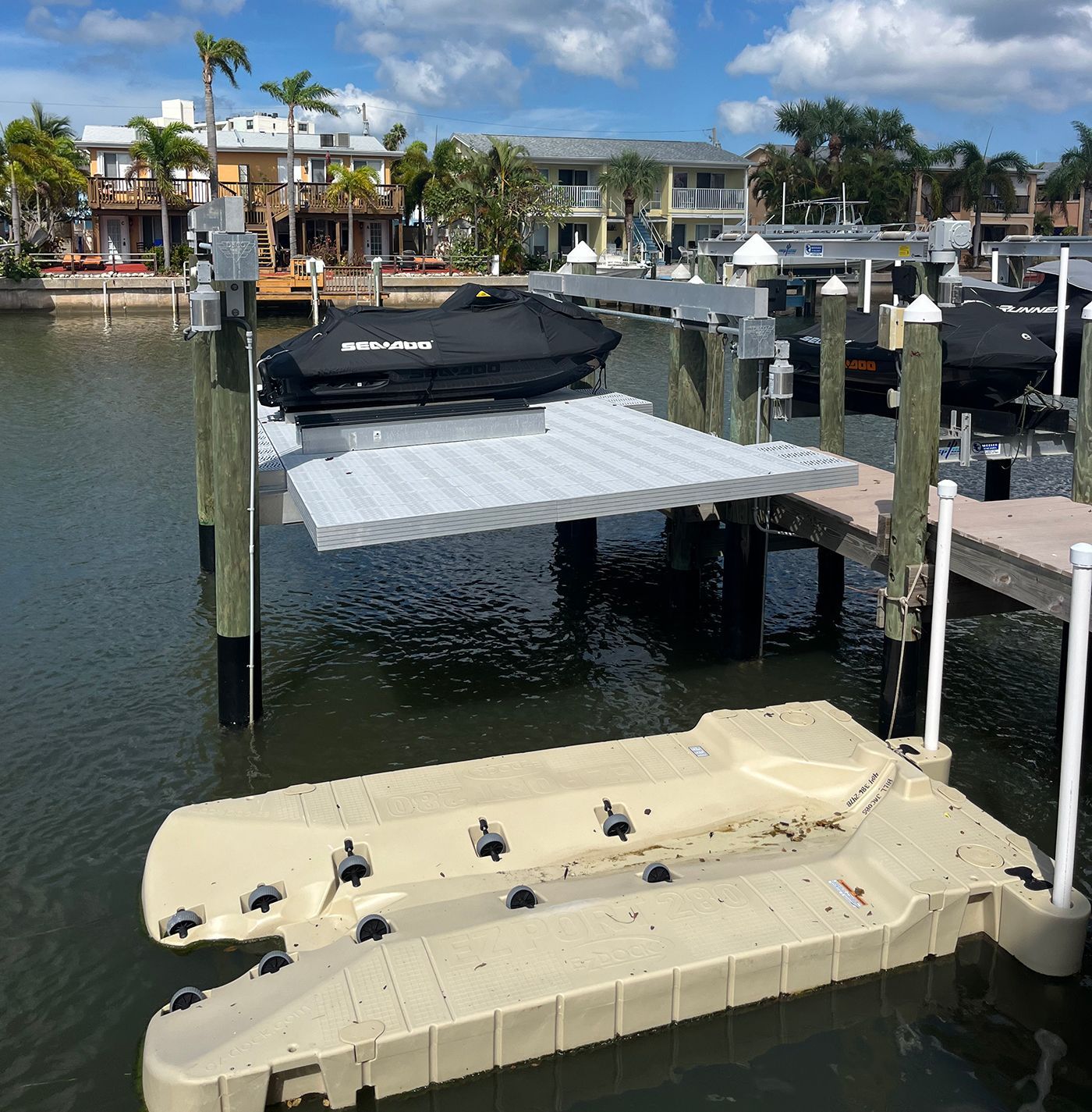 A boat lift with a jet ski on the upper platform and a floating dock below. Houses and water in the background.