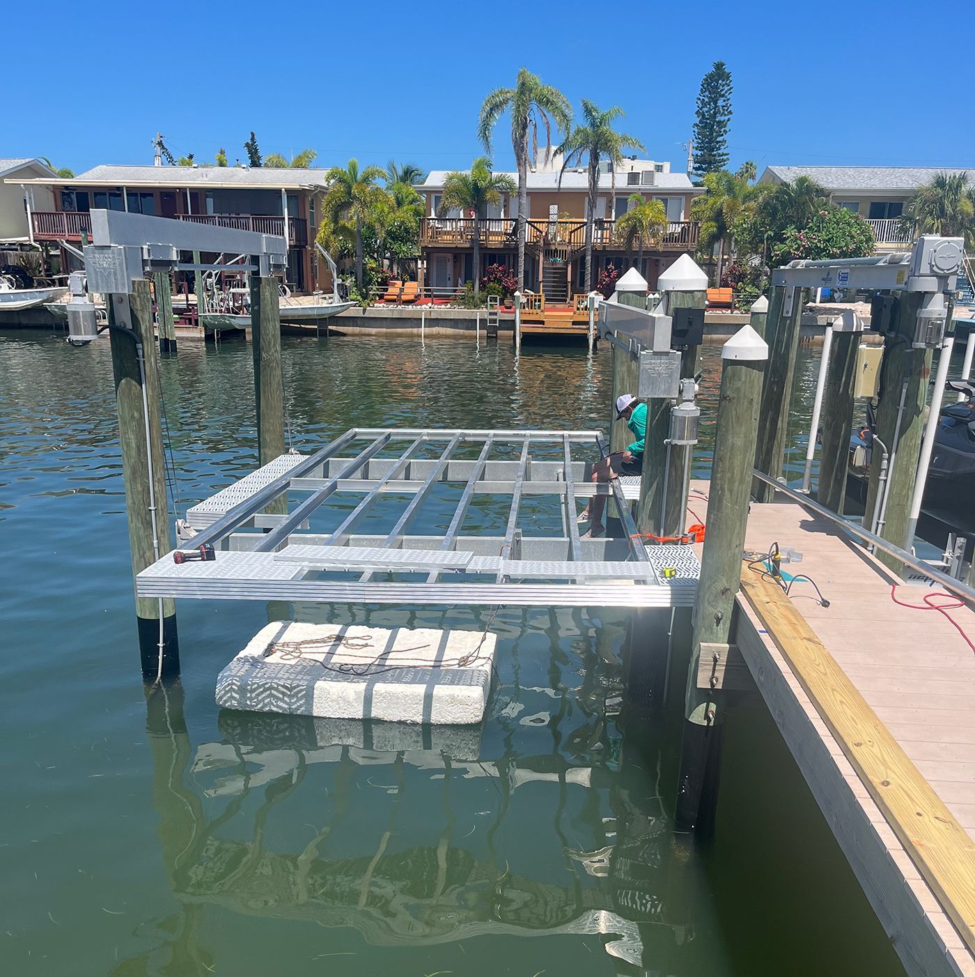 Boat lift platform in water, on a canal with houses in background.