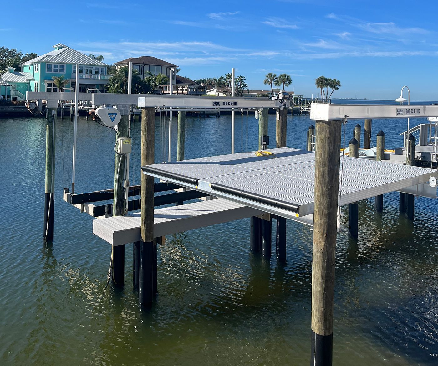 Dock with boat lift over water, houses in the background on a sunny day.