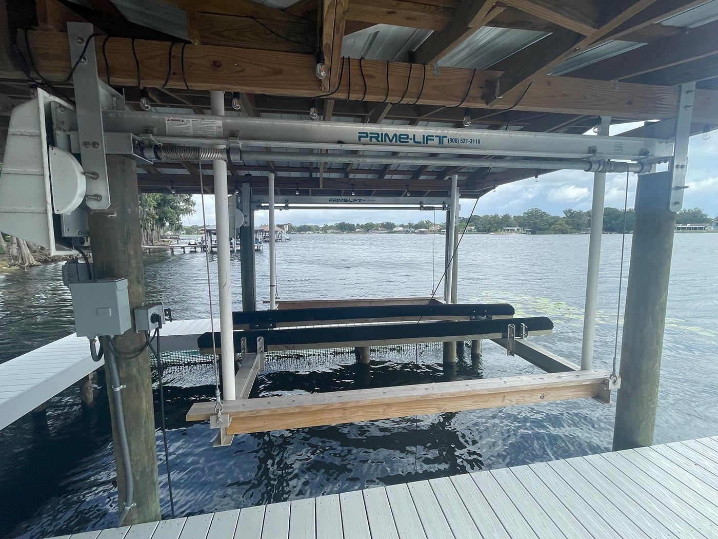 Boat lift under a dock, over water. Lift has a metal frame and wood supports.