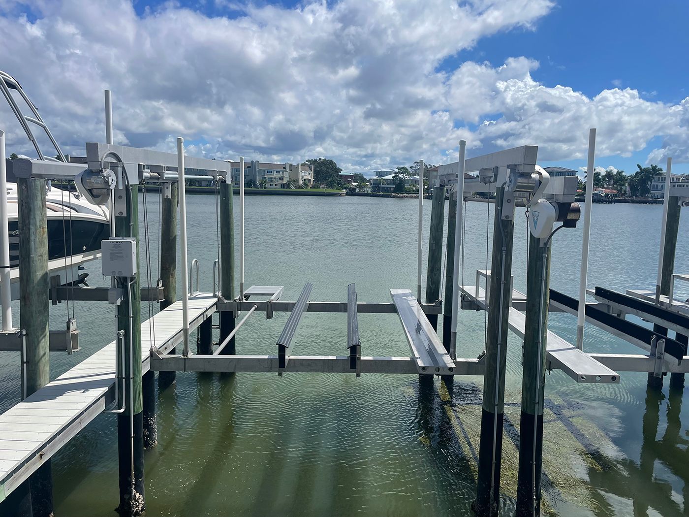 Boat lift over water, with pilings, and nearby buildings under a cloudy sky.