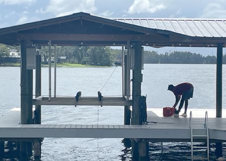 Person on dock preparing equipment near a covered boat lift over water.