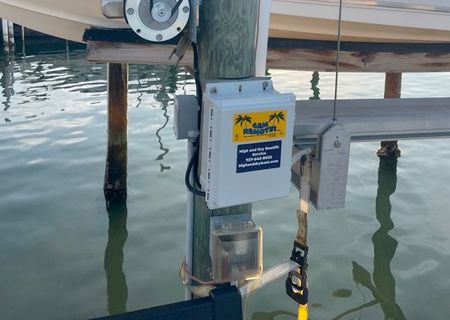 Boat lift control box on a wooden piling at a dock, next to a boat lift, over water.