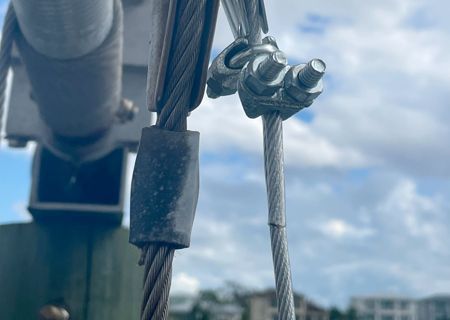 Close-up of metal cables connected with clamps against a cloudy sky.