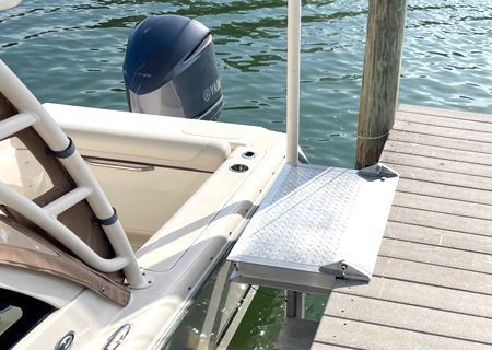 Boat next to a dock with a metal platform for boarding. Outboard motor visible.