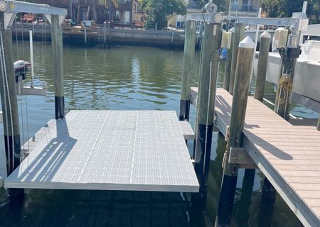 Boat lift platform at dock on waterway. Gray lift, wooden dock, pilings, and calm water.