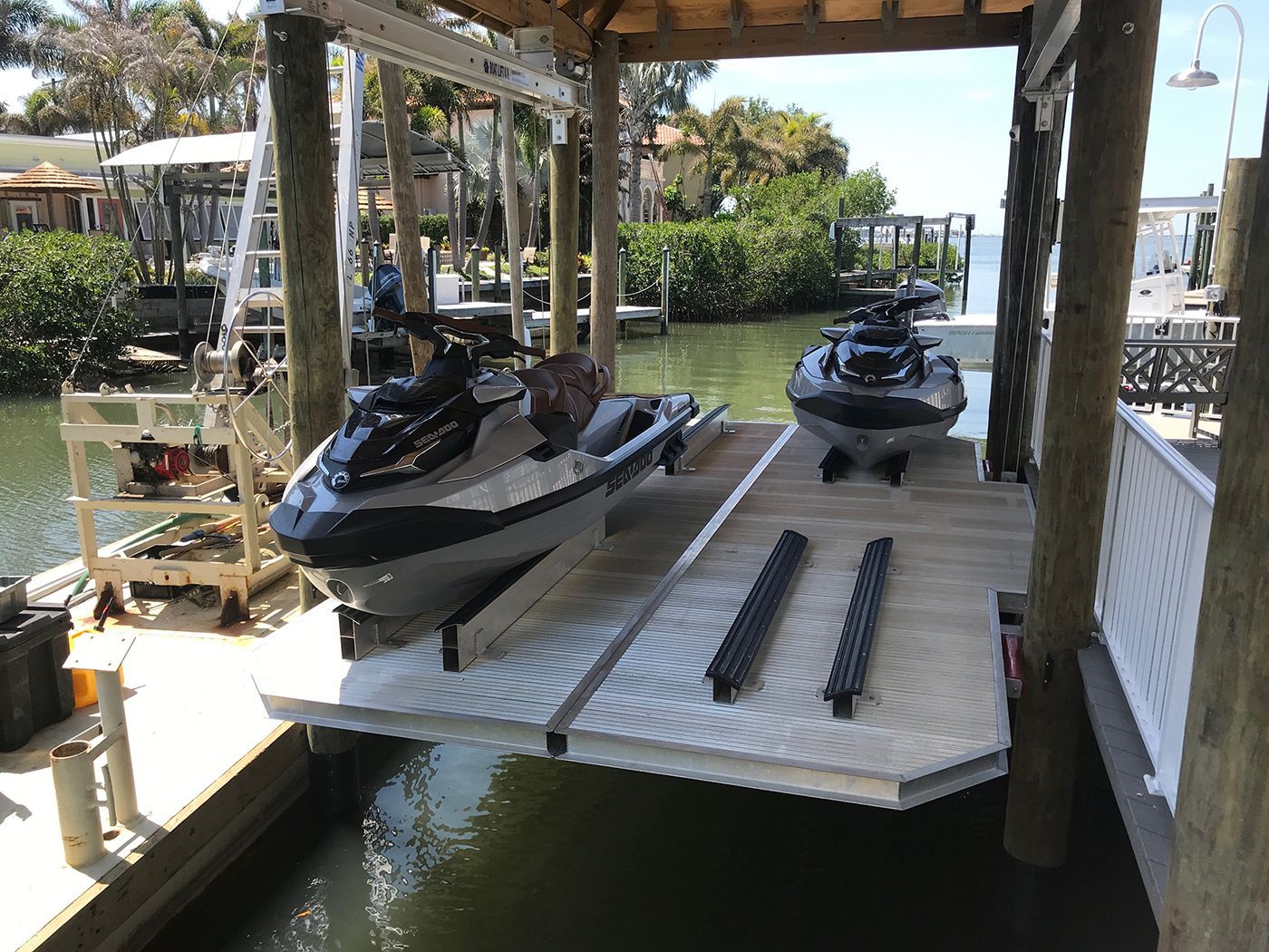 Two jet skis on a boat lift in a covered dock. Water surrounds the dock.