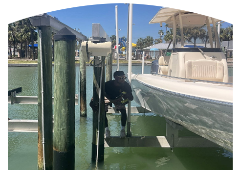 Person working on a boat lift, near a boat, dock, and water.