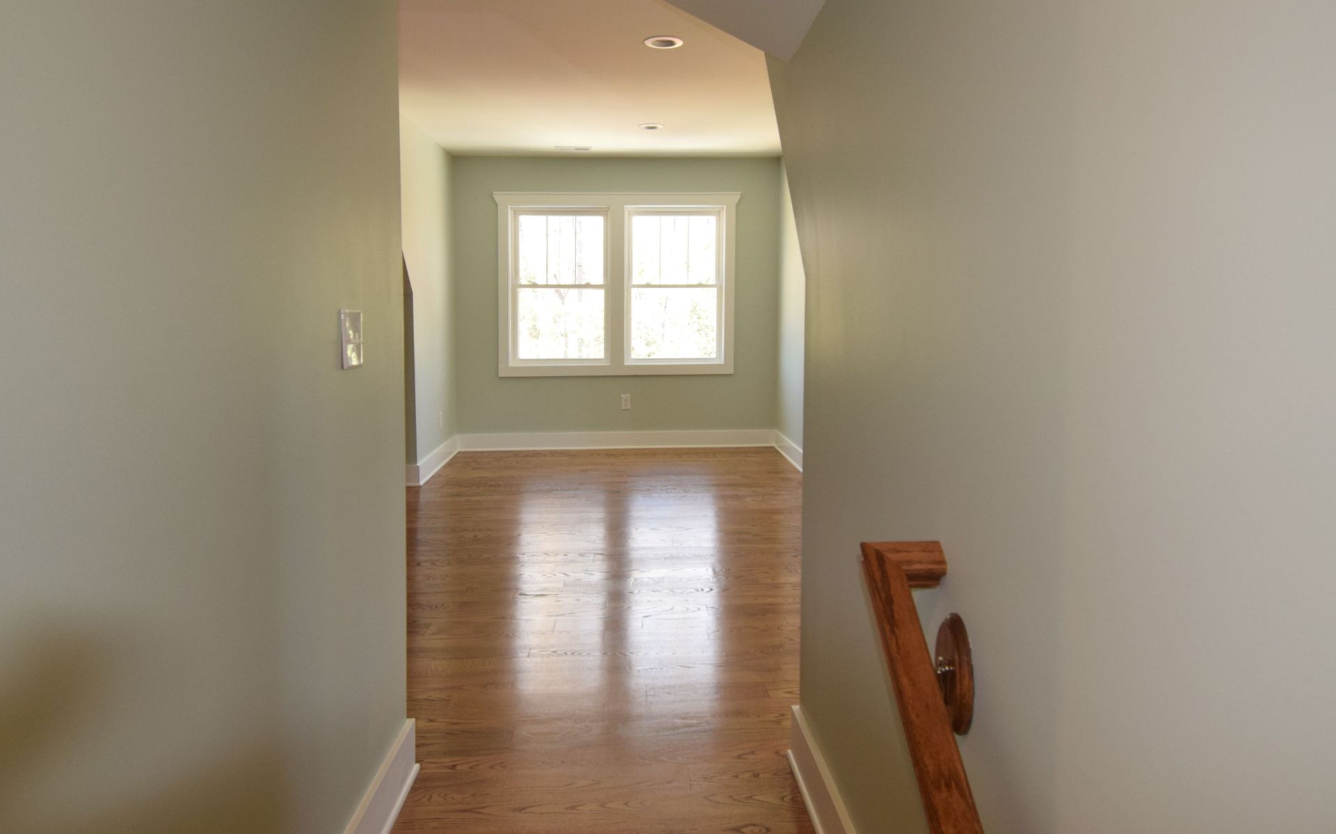 An empty hallway with hardwood floors and two windows.