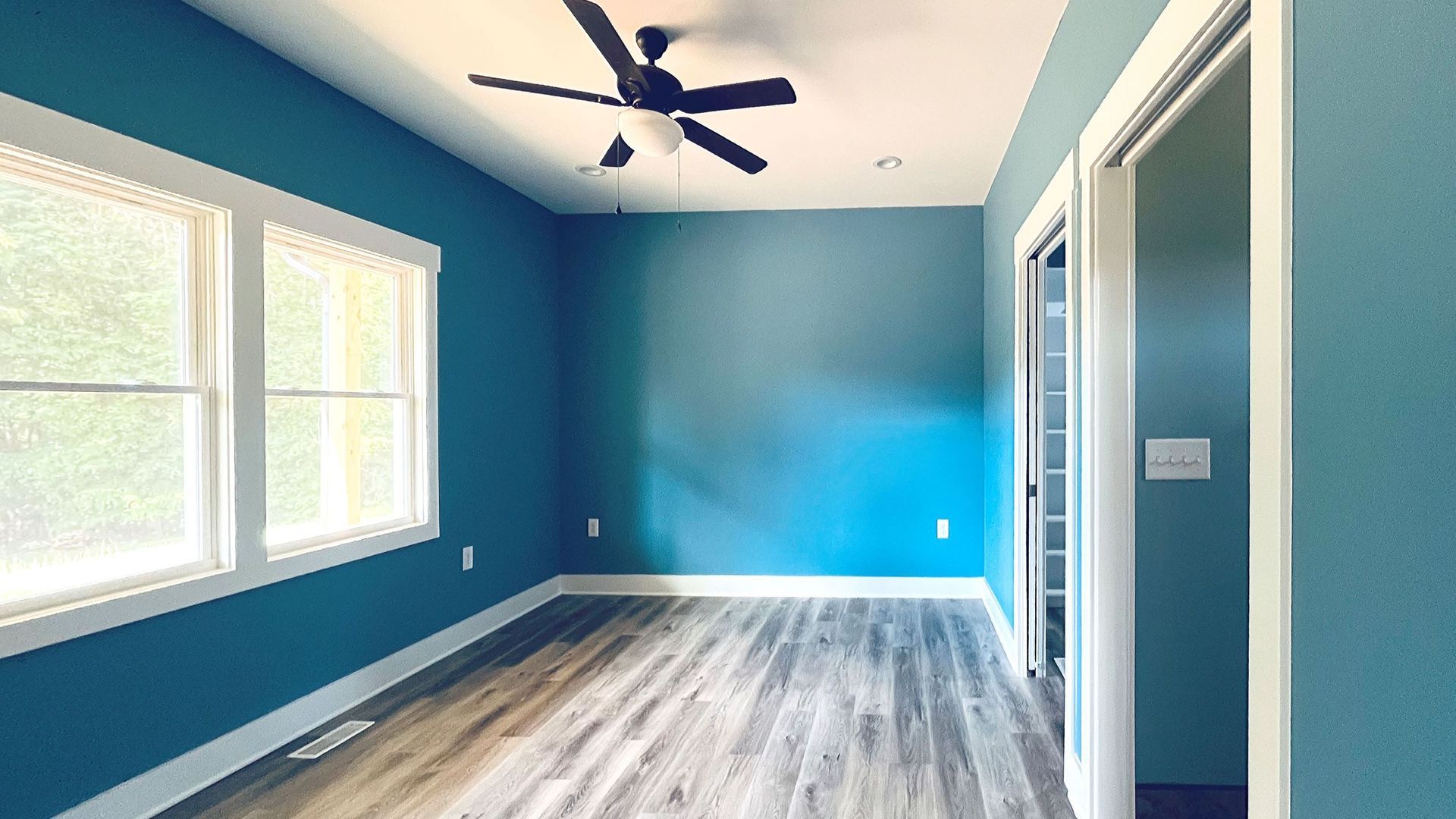An empty room with blue walls and a ceiling fan.