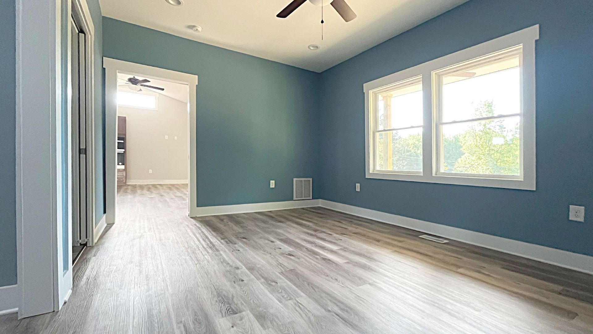 An empty room with blue walls and hardwood floors and a ceiling fan.