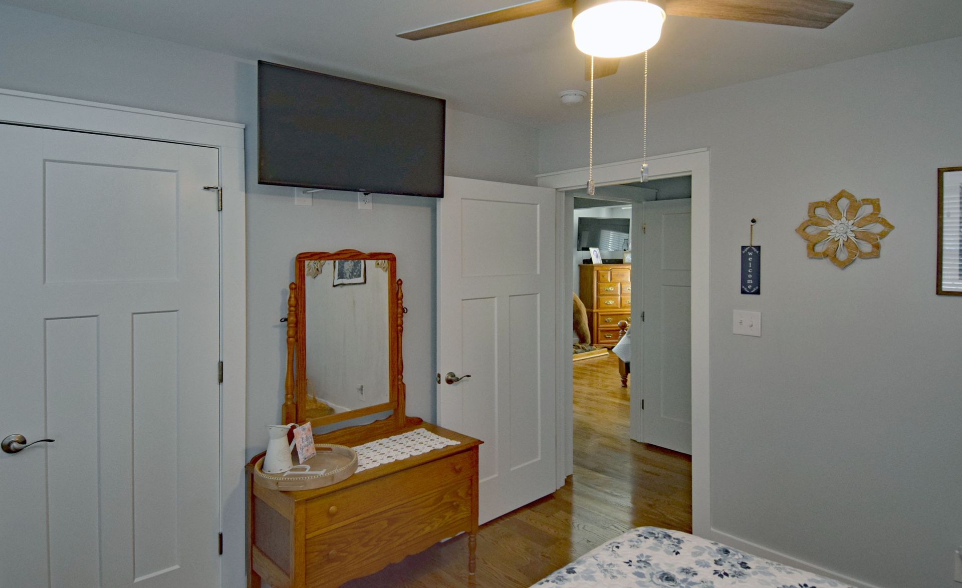A bedroom with a dresser , mirror , television and ceiling fan.