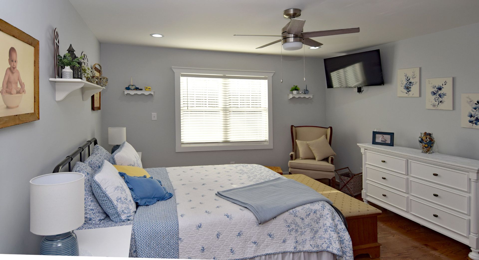A bedroom with a bed , dresser , chair and ceiling fan.