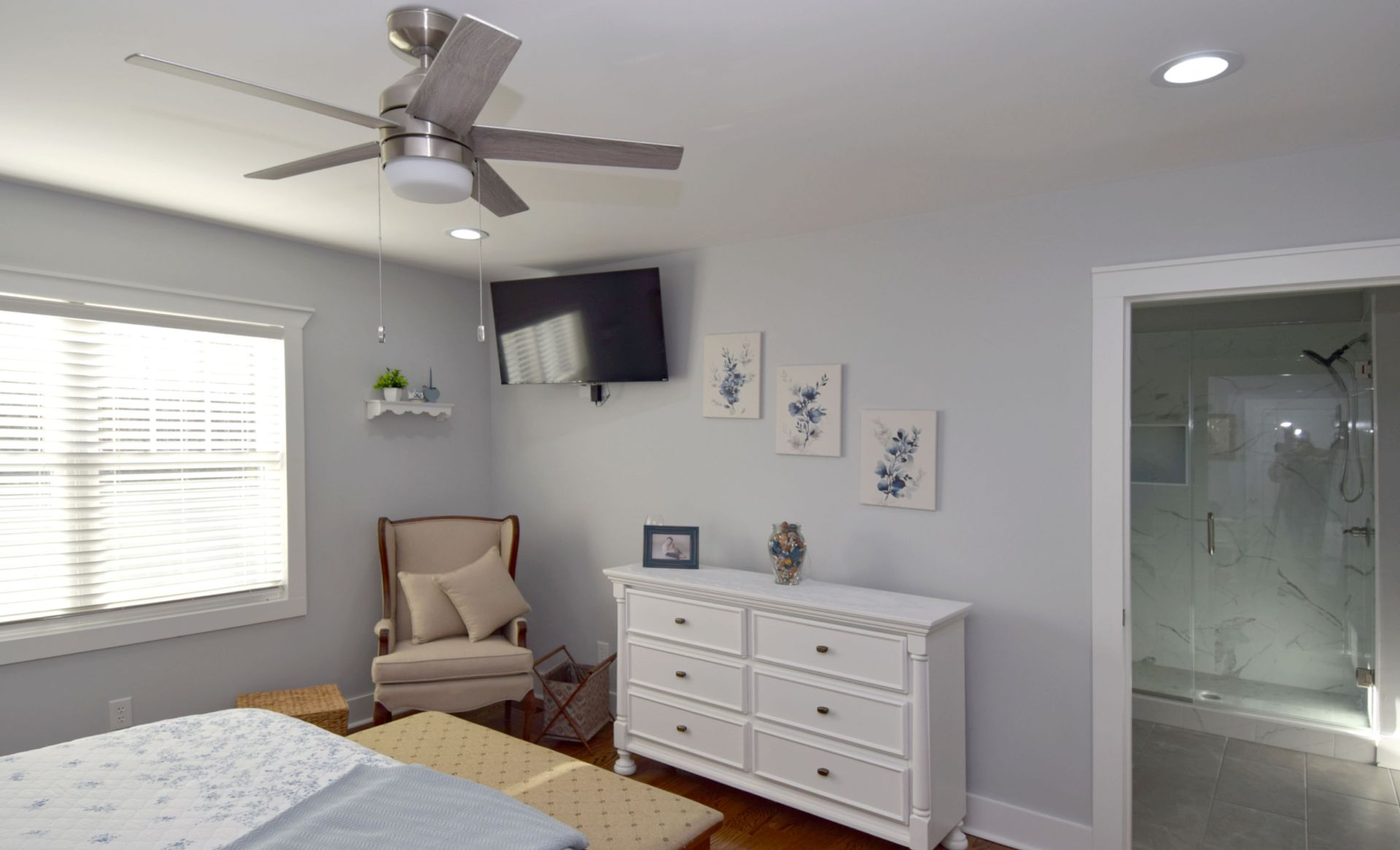 A bedroom with a bed , dresser , chair and ceiling fan.