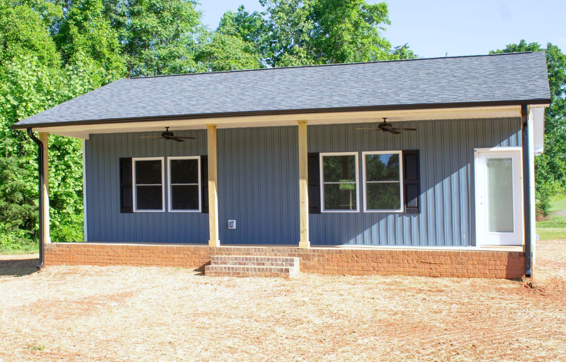 A small blue house with a porch and a roof is sitting on top of a dirt field.