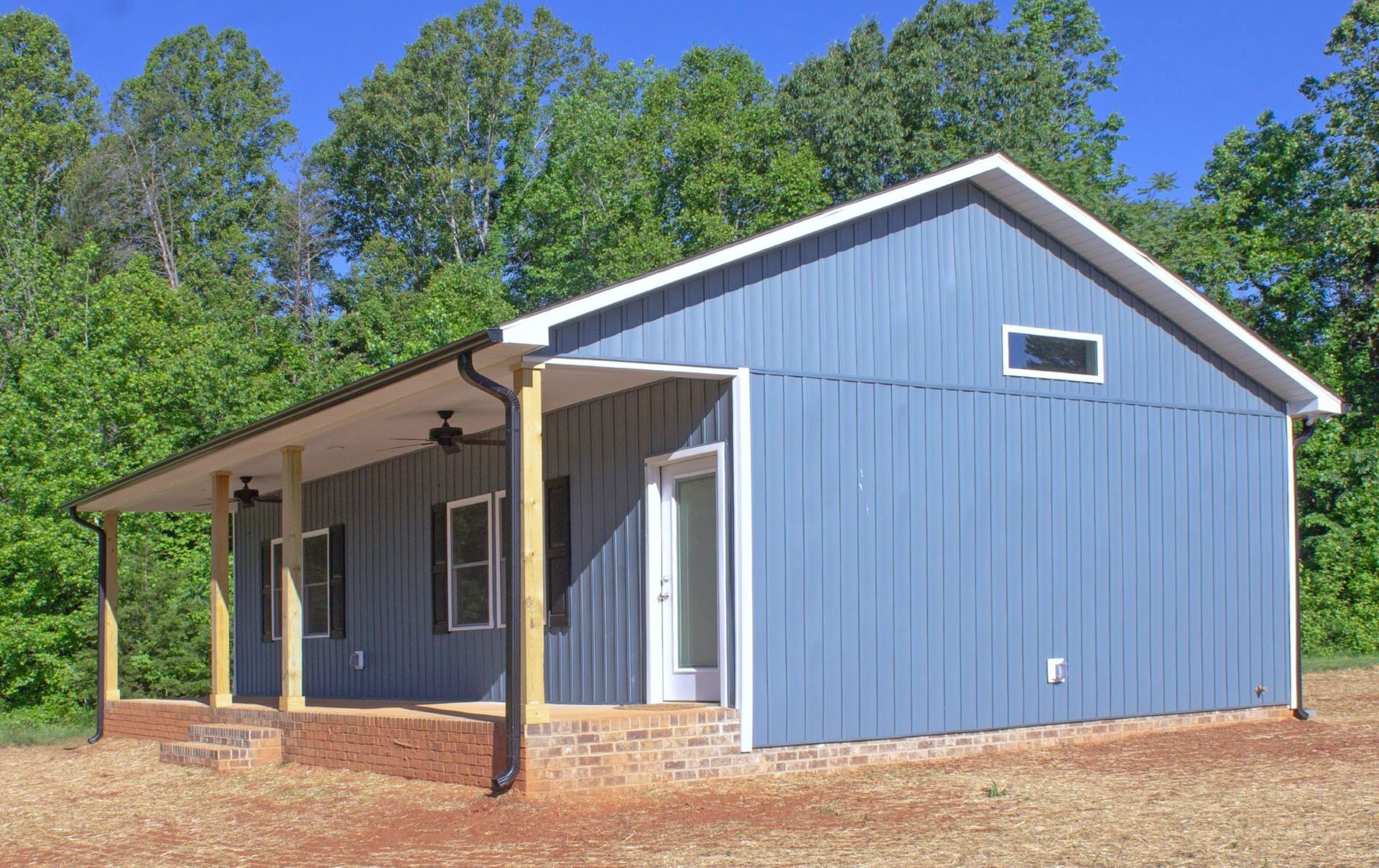 A blue house with a porch and trees in the background
