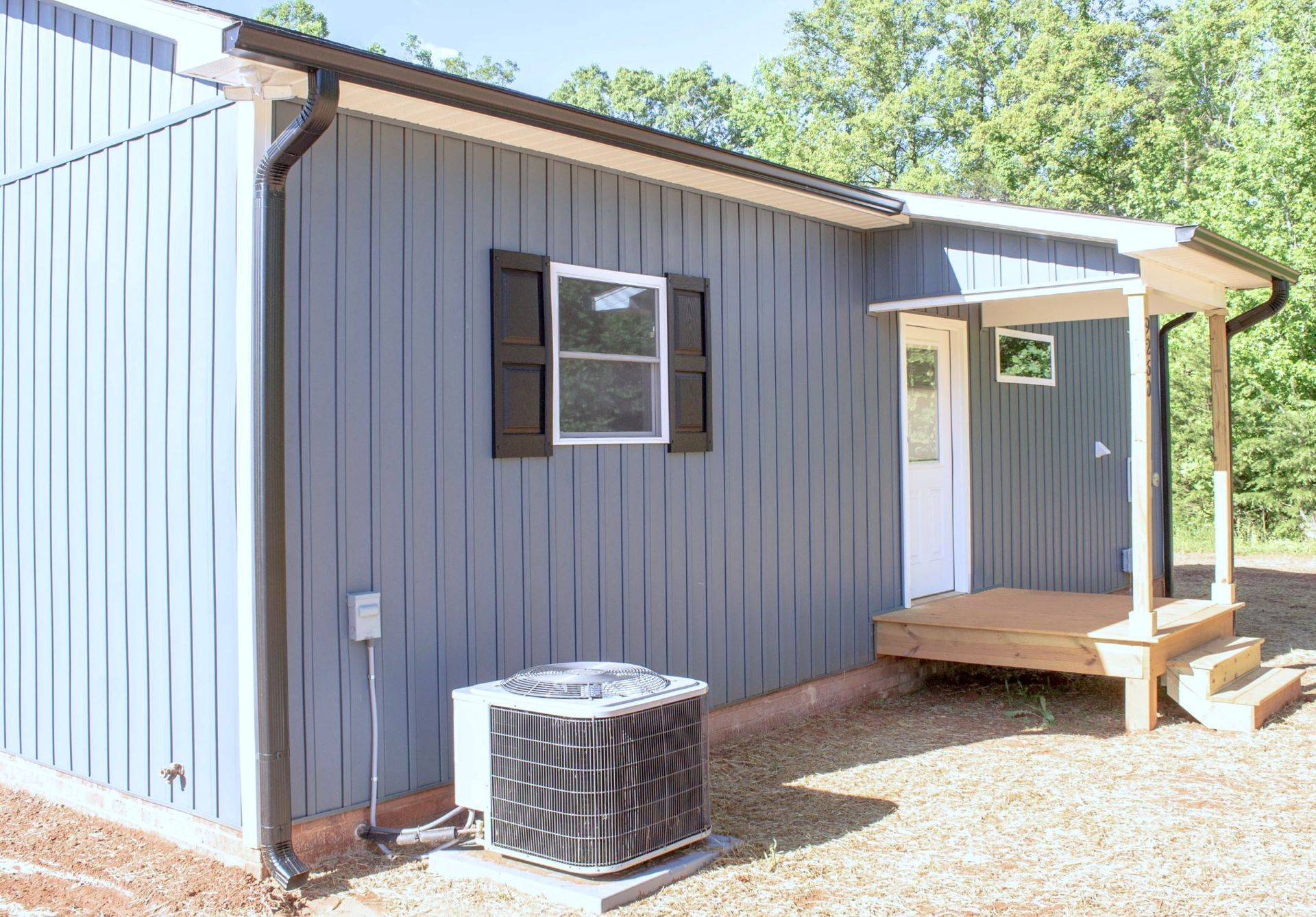 A small house with a porch and an air conditioner on the side of it.