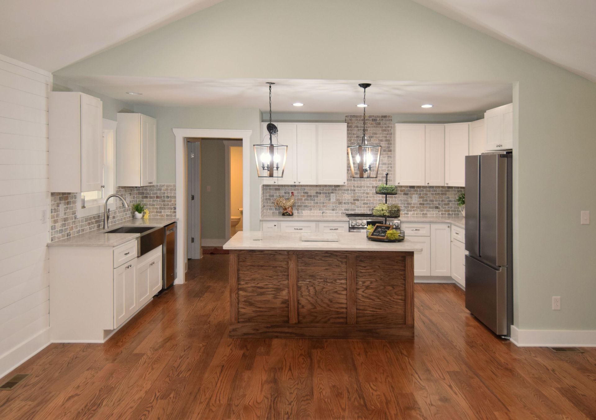 A kitchen with white cabinets , stainless steel appliances , hardwood floors and a large island.