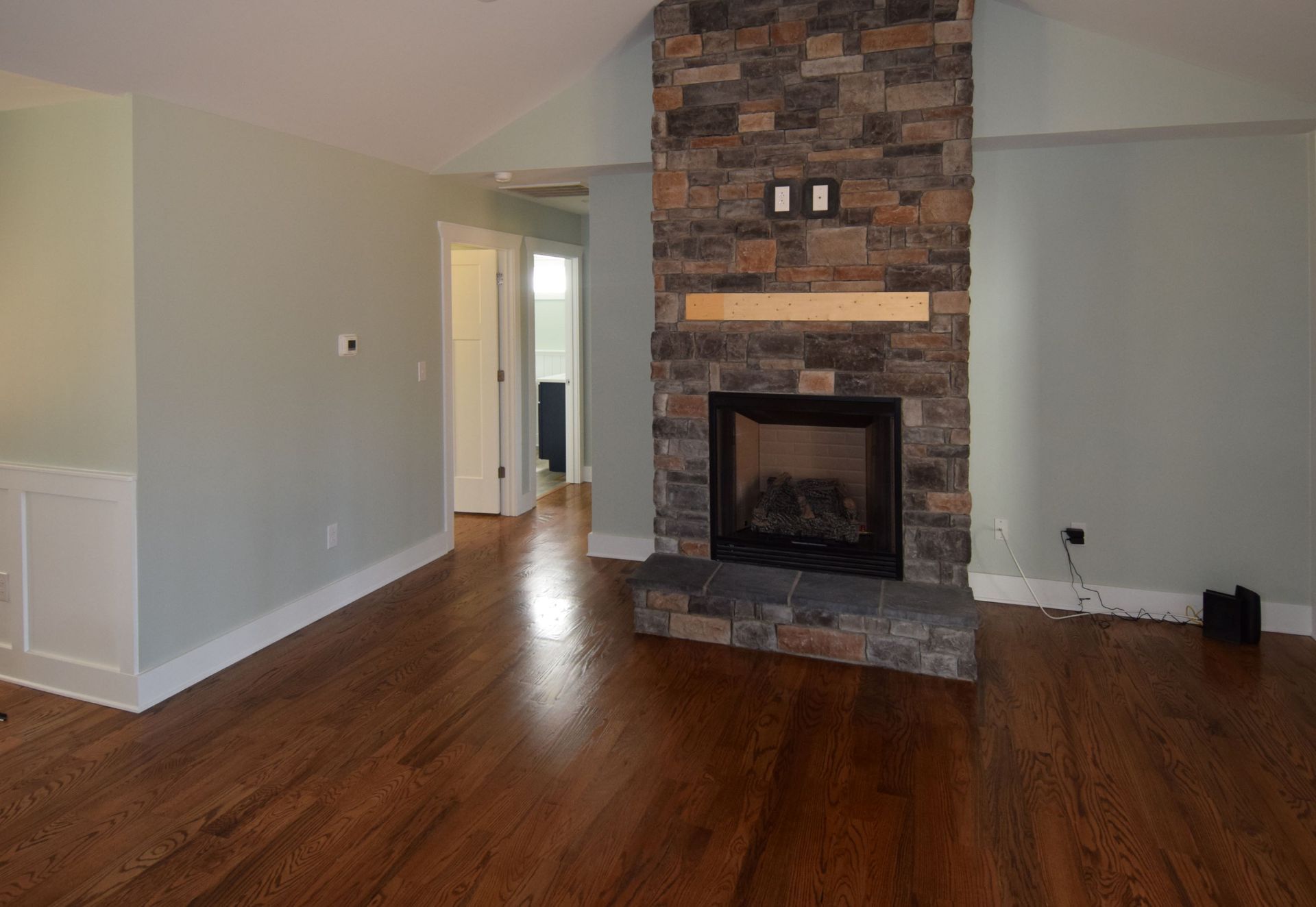 An empty living room with a stone fireplace and hardwood floors.