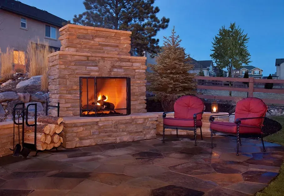 There is a fireplace in the backyard with two chairs and a table.