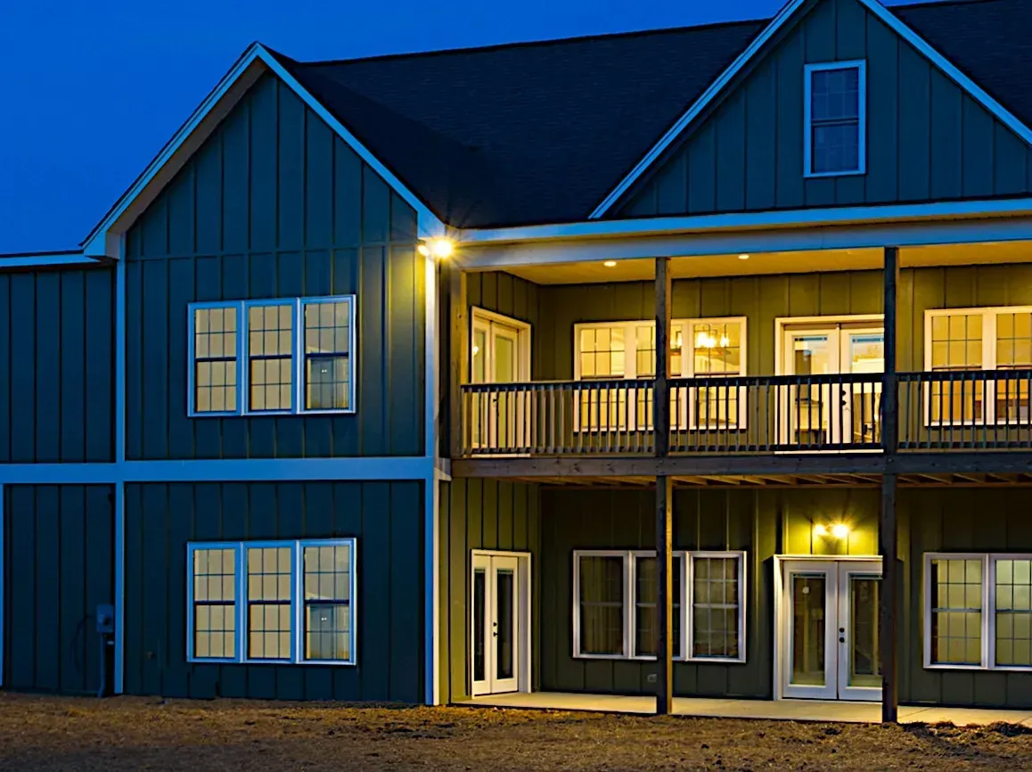 A large green house with a balcony is lit up at night.