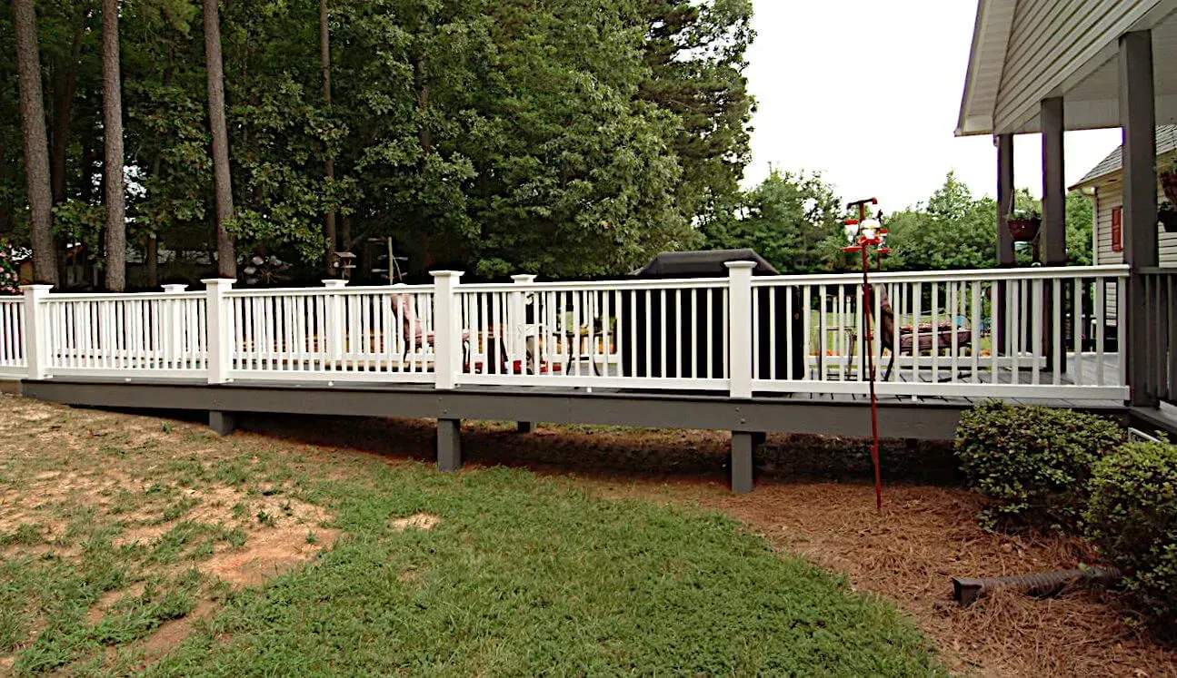 A large white deck with a grill on it is in the backyard of a house.