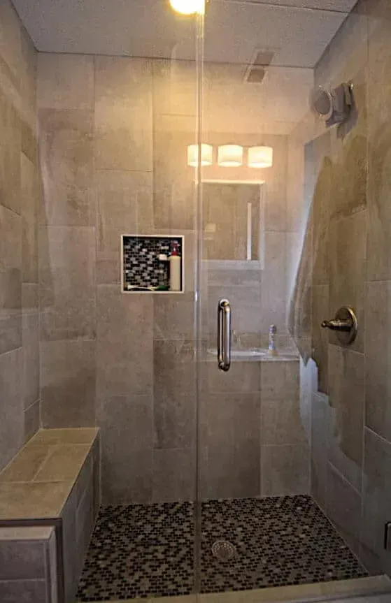 A bathroom with a walk in shower with a glass door and a bench.