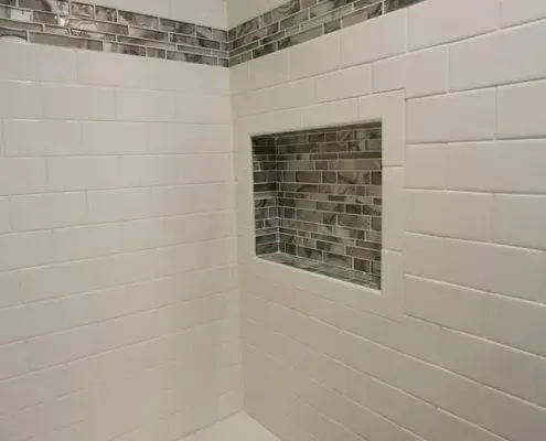 A shower with white tiles and a niche in the wall.