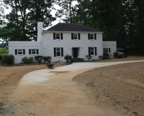 A white house with black shutters and a wheelbarrow in front of it
