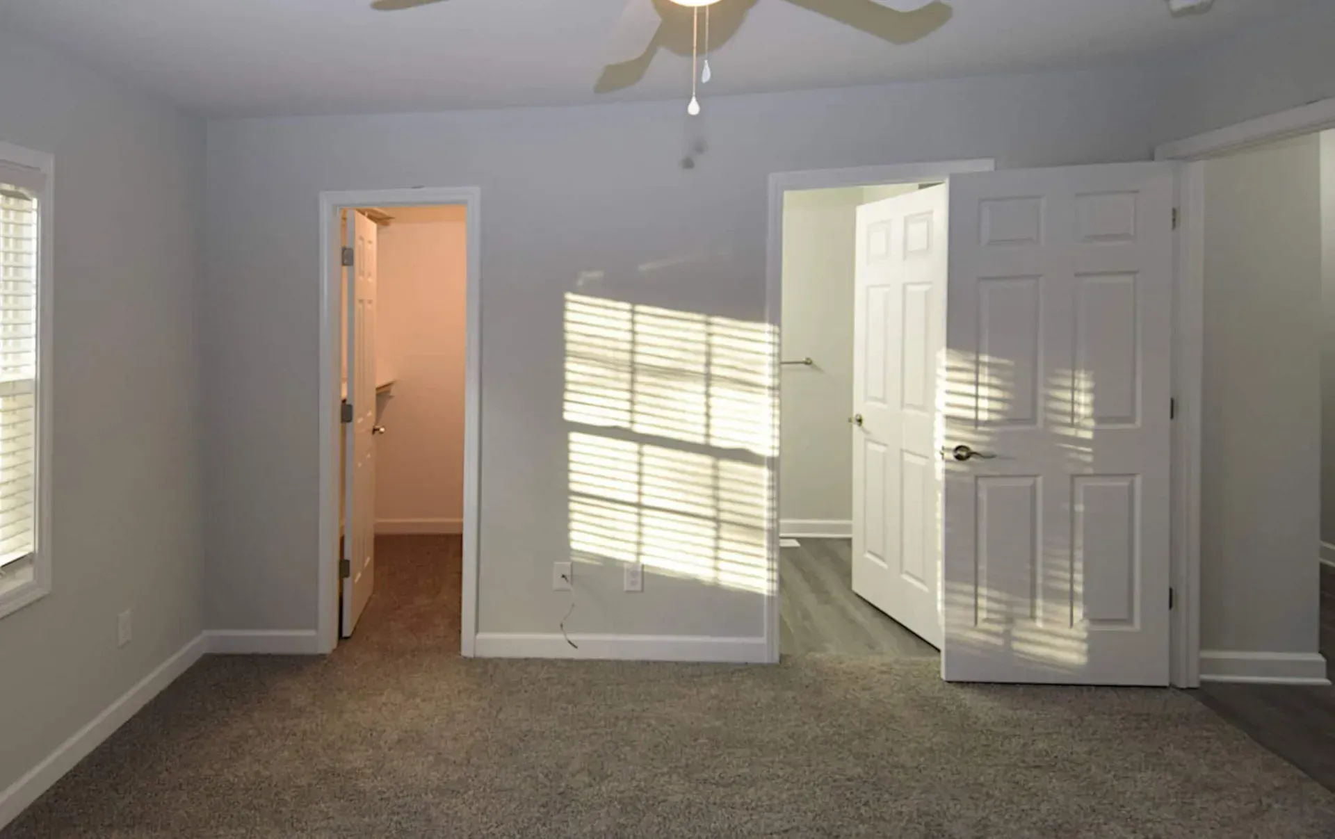 An empty bedroom with a ceiling fan and a window.