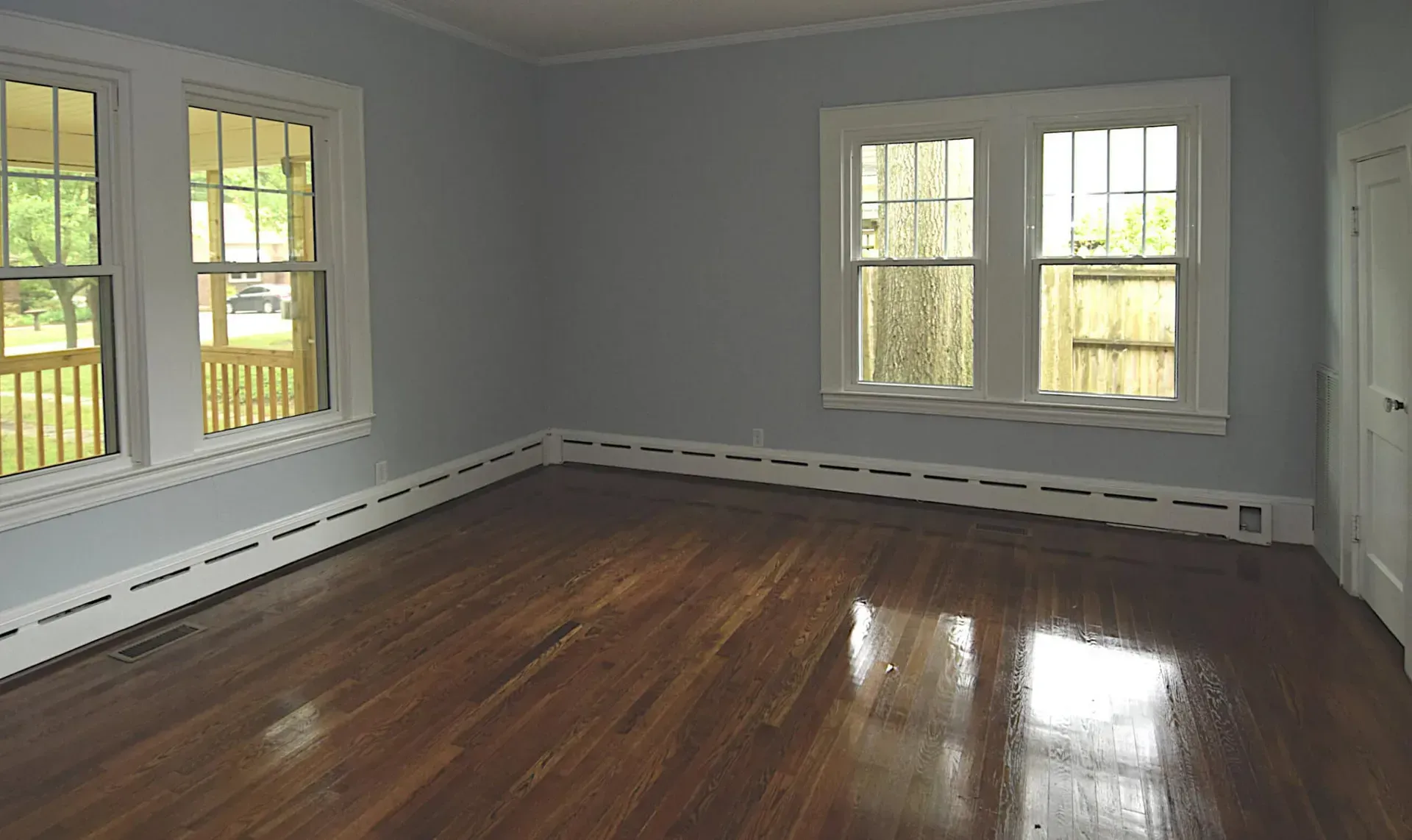 An empty room with hardwood floors and two windows