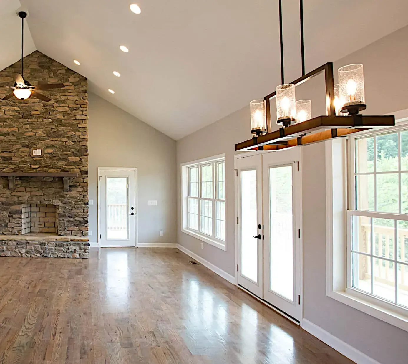 An empty living room with hardwood floors and a stone fireplace