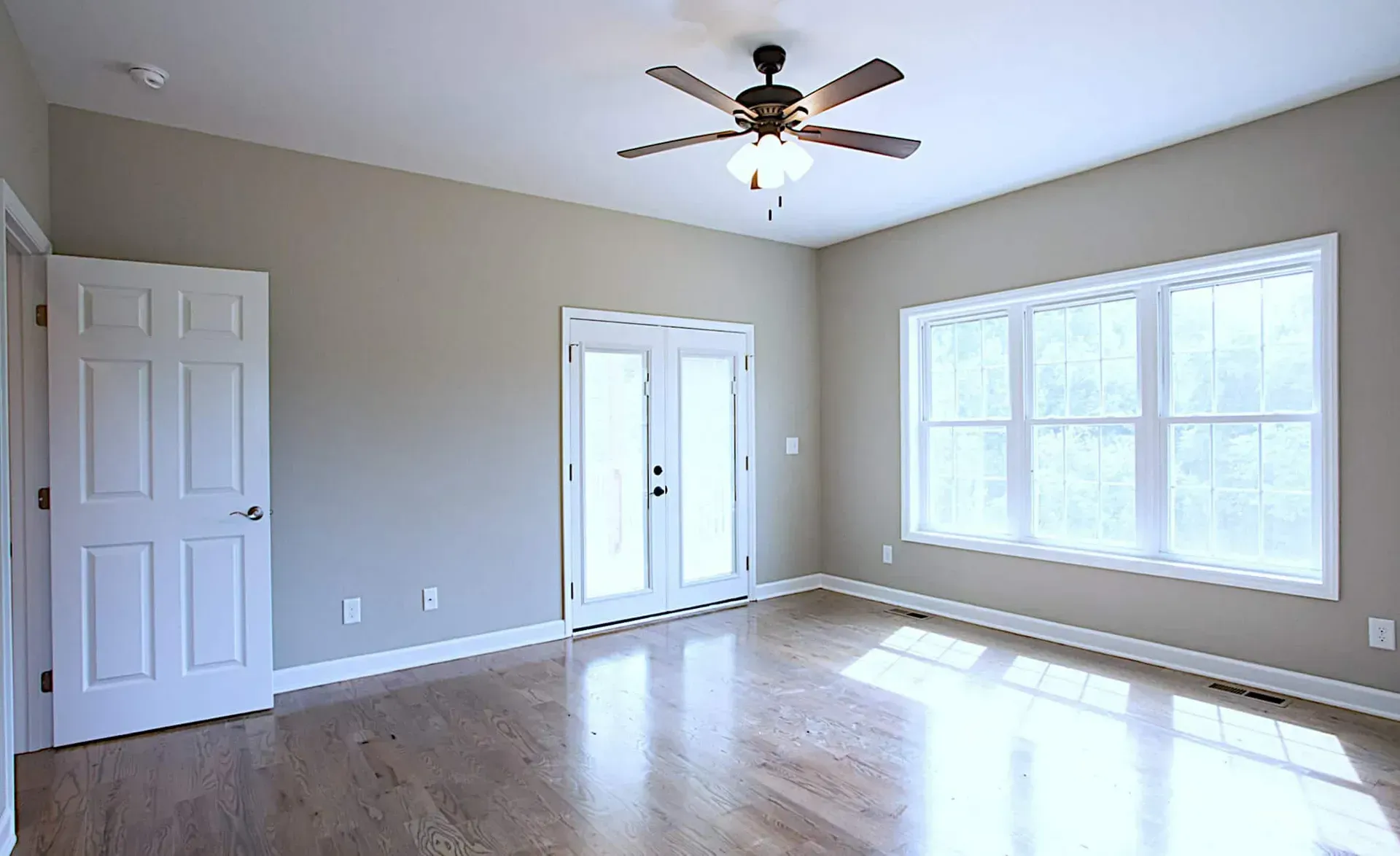 An empty room with hardwood floors and a ceiling fan.