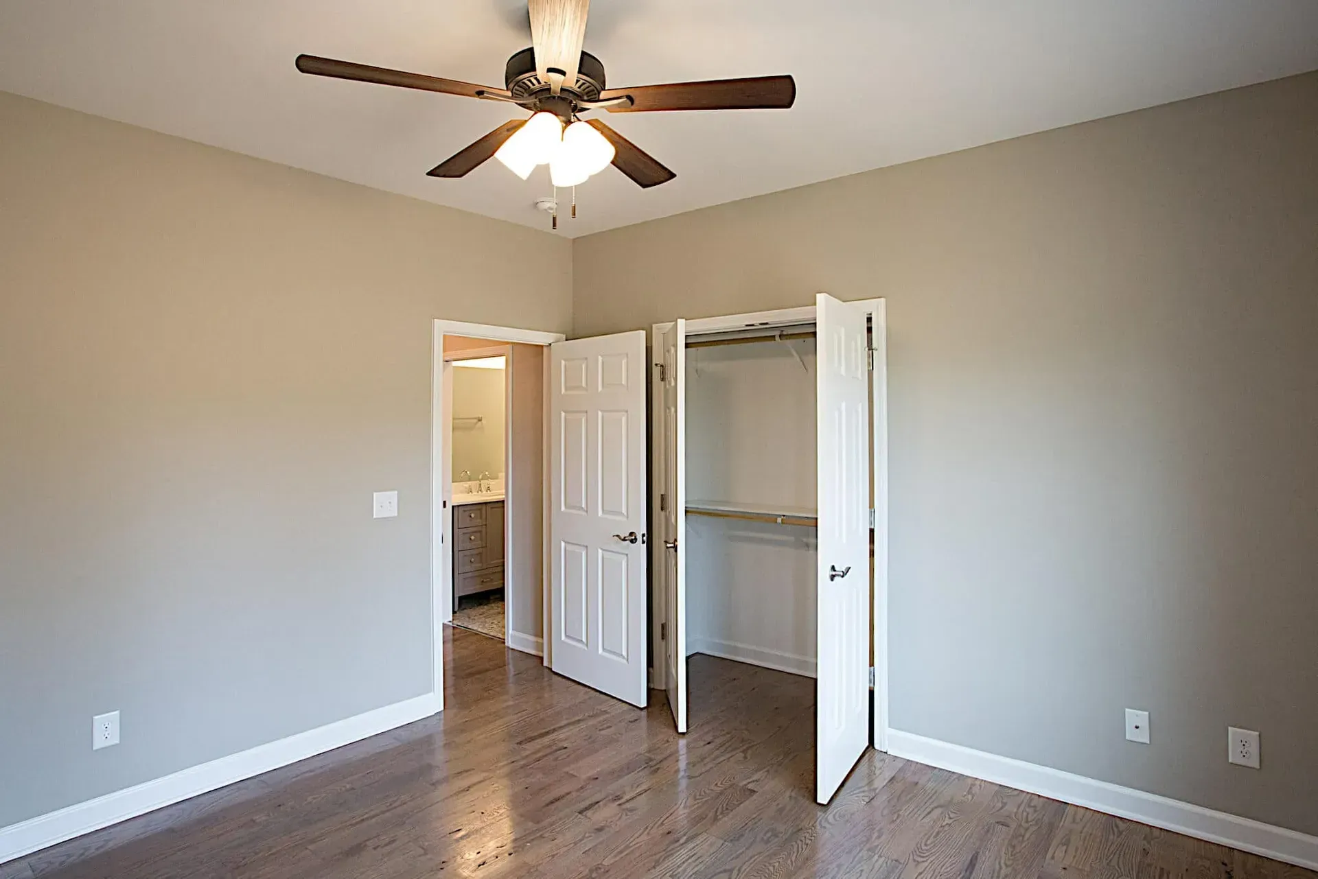 An empty bedroom with hardwood floors and a ceiling fan.