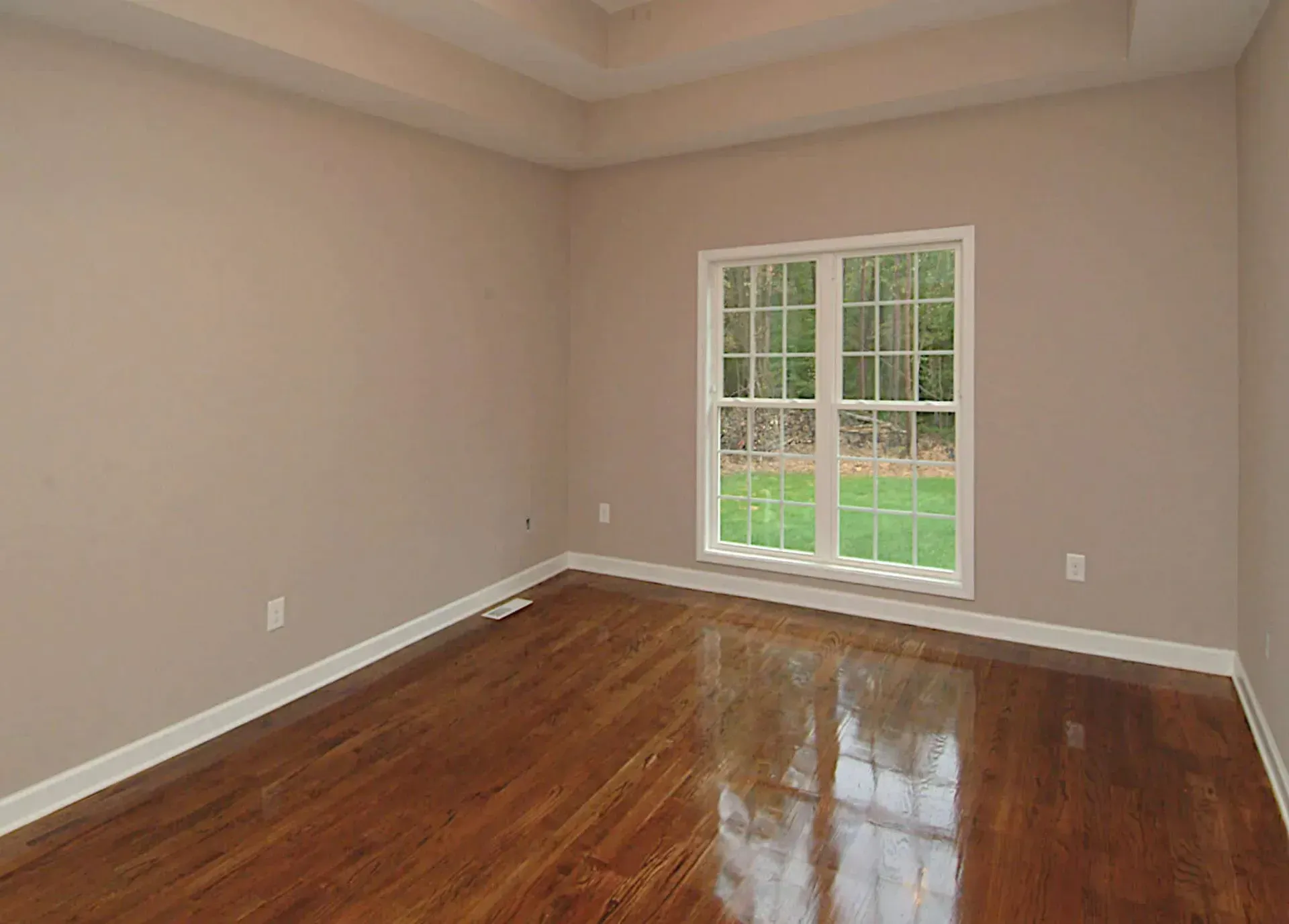 An empty room with hardwood floors and two windows.