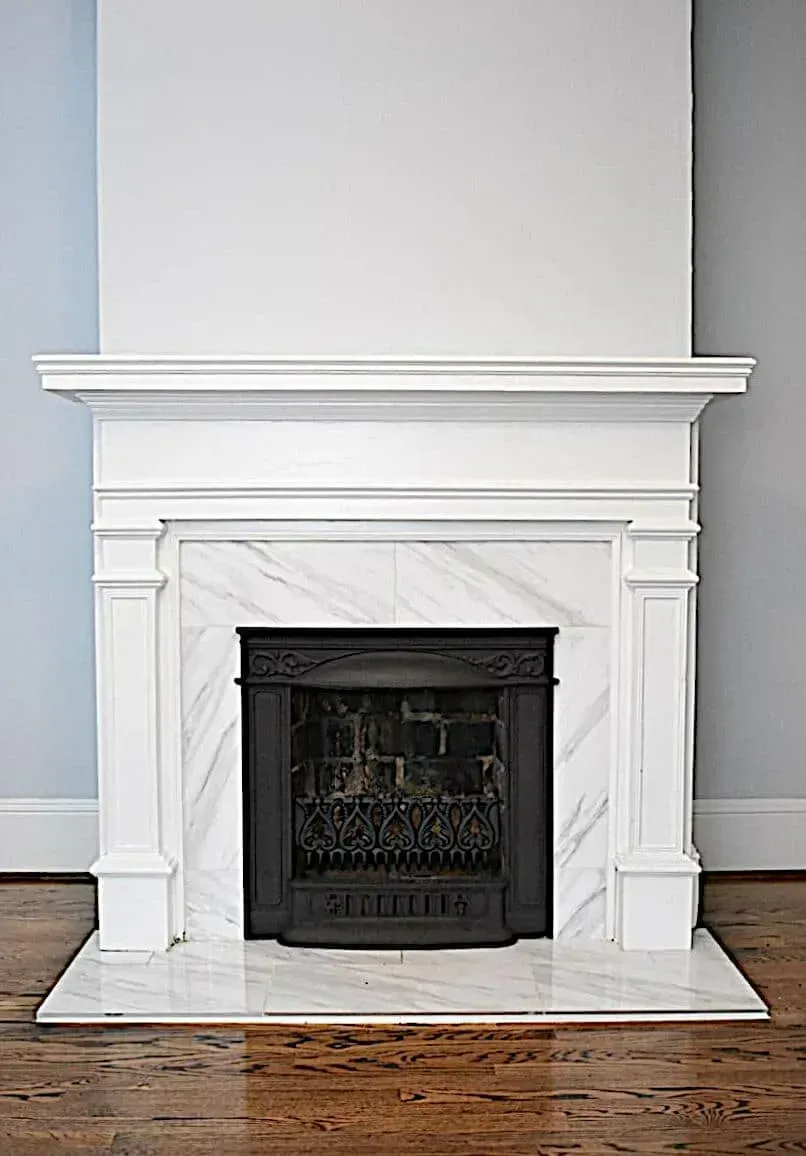 A fireplace with a white marble mantle and a wooden floor in a living room.
