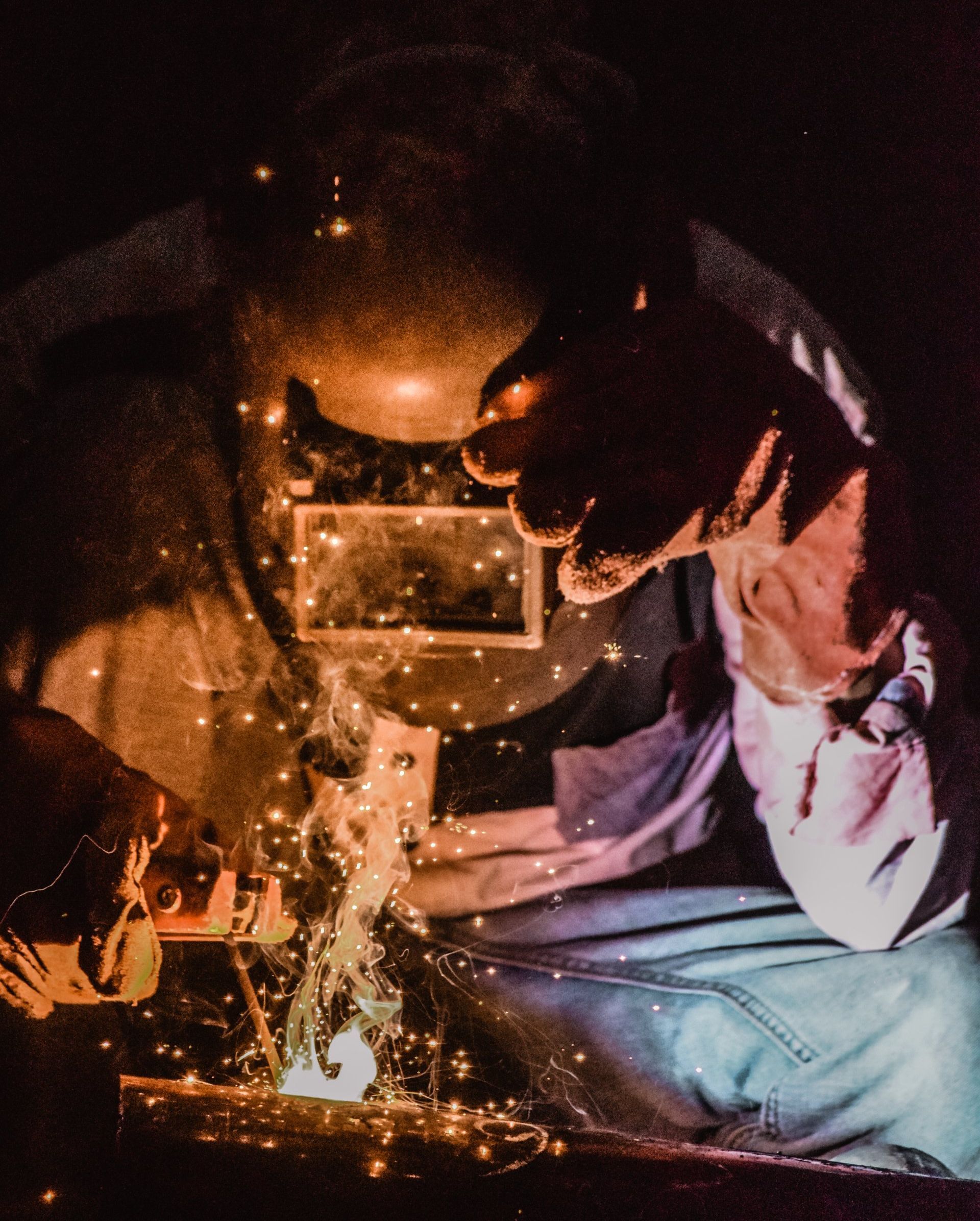 A man wearing a welding mask is welding a piece of metal.