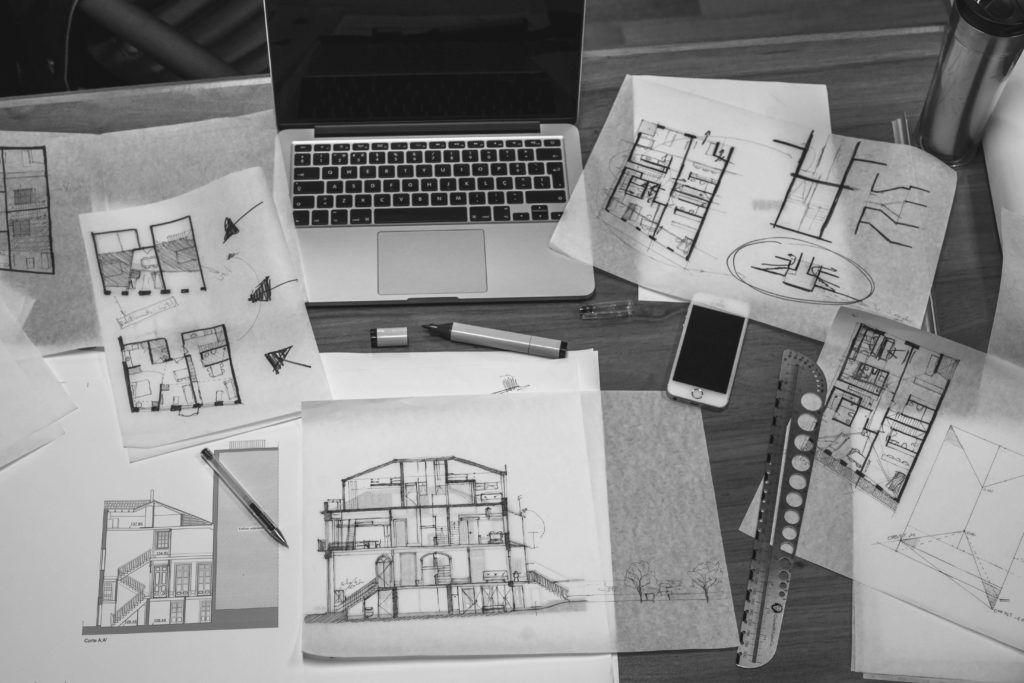 A black and white photo of a desk with drawings and a laptop.