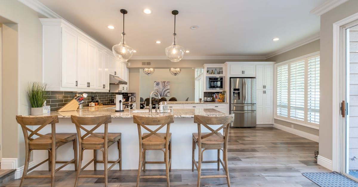 A kitchen with a large island , stools and a refrigerator.