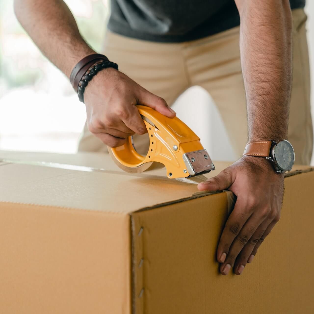 A man is taping a cardboard box with a yellow tape dispenser.