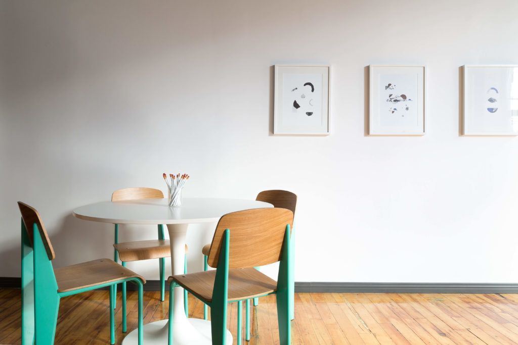 A dining room with a table and chairs and paintings on the wall.