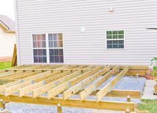 Wooden deck framework under construction near a house with two windows.