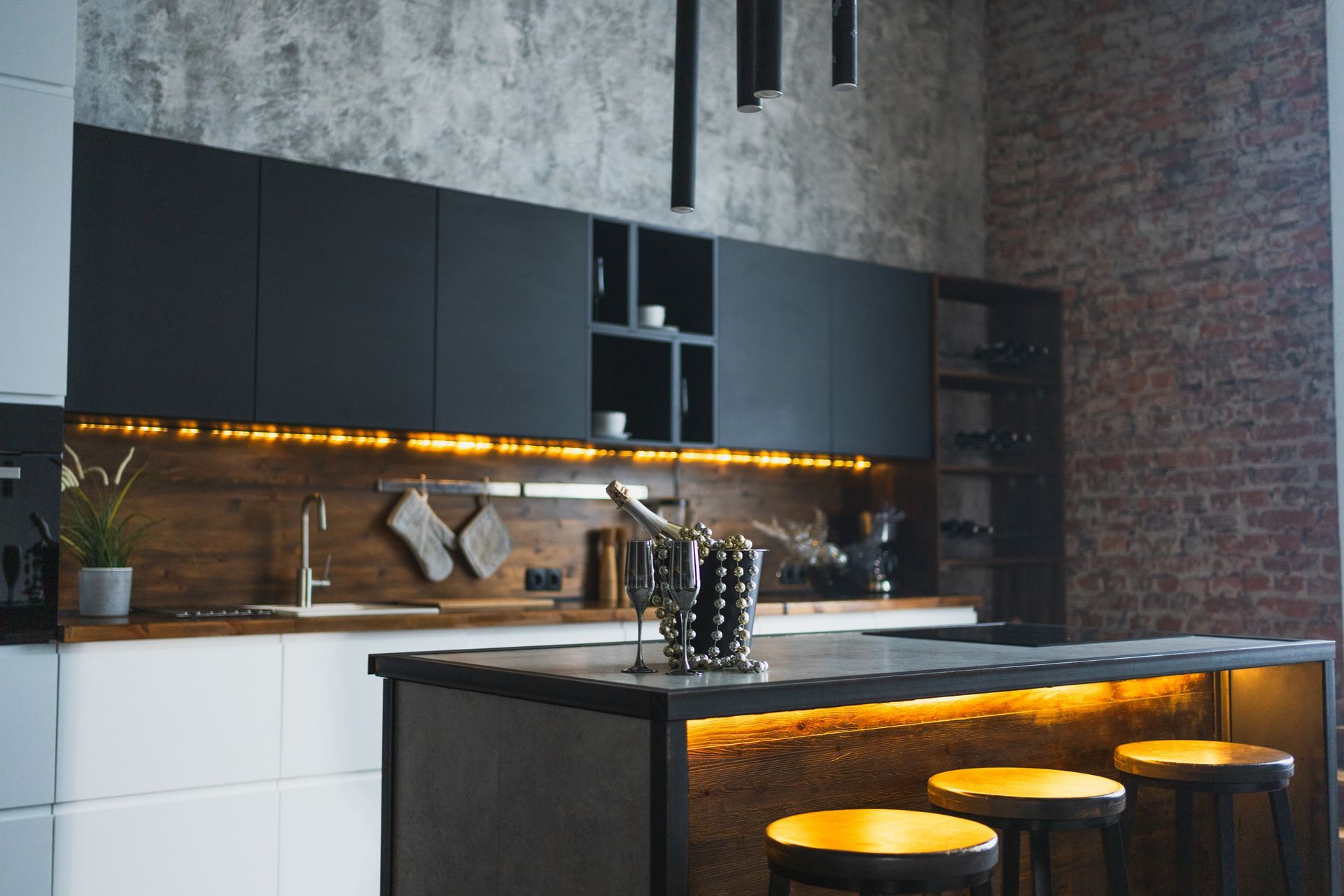 Modern kitchen with black cabinets, brick accent wall, and bar with stools, lit with warm light.