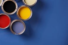 Open paint cans in red, black, yellow, and blue hues on a blue surface.