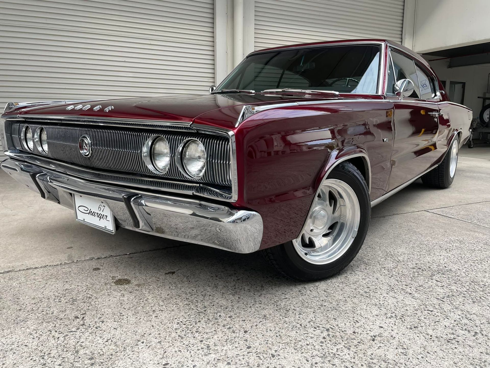 A red dodge charger is parked in front of a garage door.