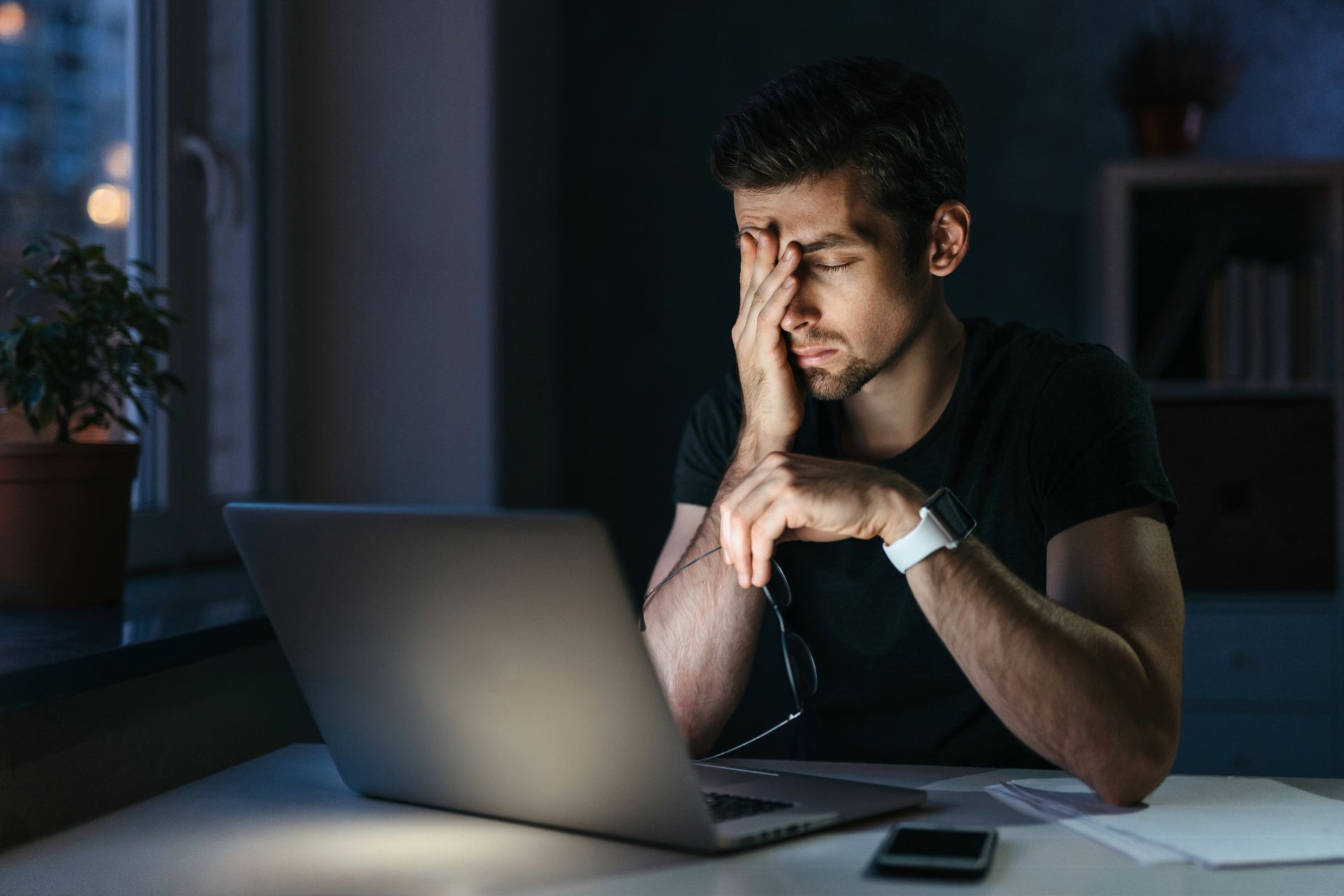 Young businessman at laptop with a headache. It's nighttime. He's stressed and tired.