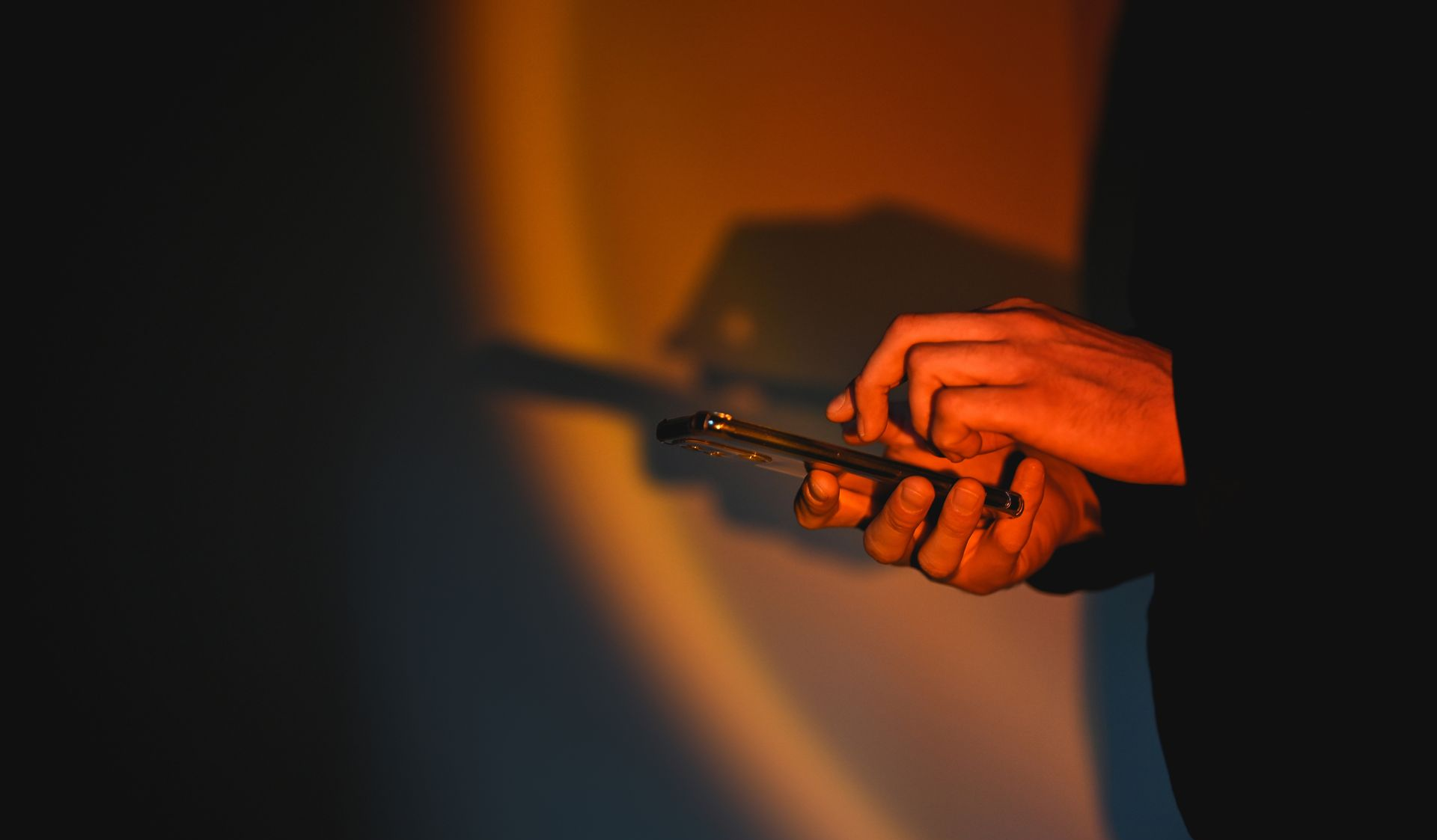 Hands using mobile phone in warm sunlight. Shadow of hands in bakground.