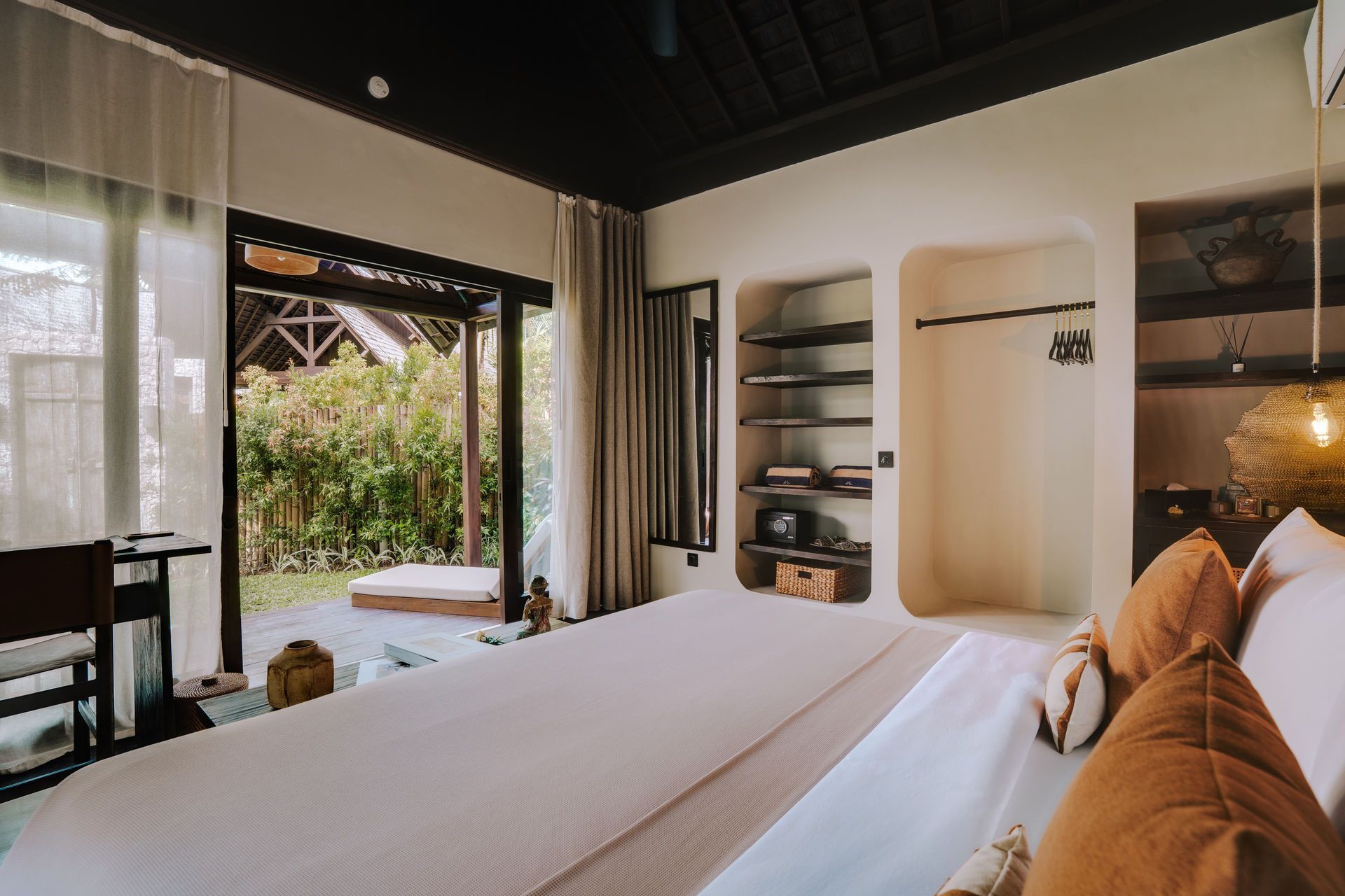 Modern bedroom with a large bed, built-in shelves, and open doors to a lush garden patio.