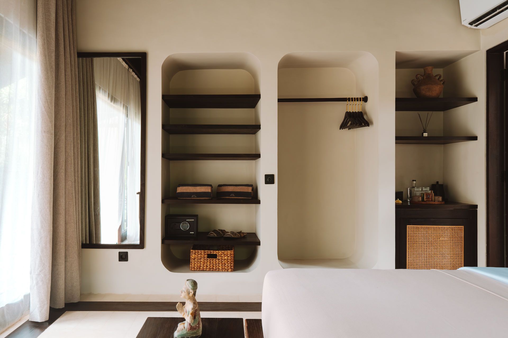 Minimalist bedroom with built-in shelves, mirror, beige walls, and a partially visible bed